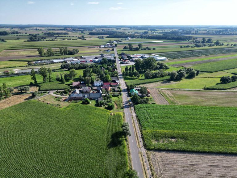 Fotografia lotnicza przedstawiająca zabudowania miejscowości w otoczeniu licznych zielonych pól.