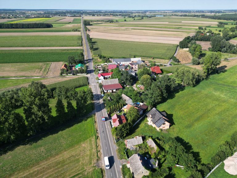 Fotografia lotnicza przedstawiająca zabudowania miejscowości w otoczeniu licznych zielonych pól.