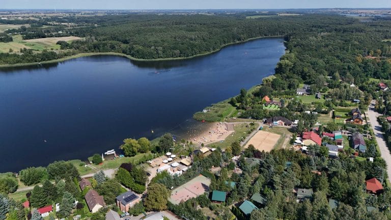 Fotografia lotnicza przestawiająca jezioro Cichowo. Dużą część wokół jeziora zajmuje las, a na pierwszym planie widać liczne zabudowania.