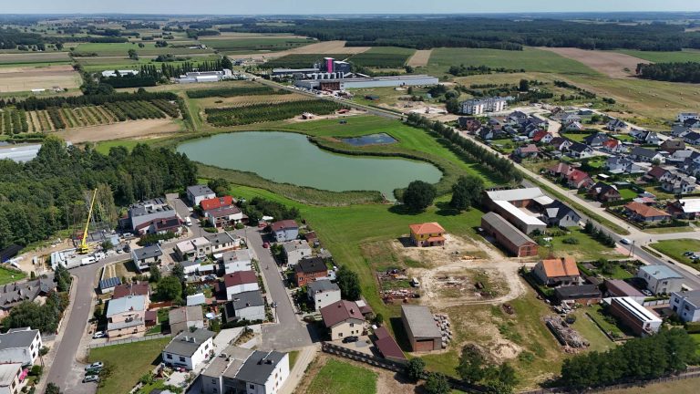 Fotografia lotnicza przedstawiająca Krzywiń. W oczy rzuca się jezioro z małym zbiornikiem retencyjnym obok. Widać zabudowę mieszkalną a na horyzoncie można zauważyć przemysłową część miasta. Miasto jest otoczone licznymi drzewami, łąkami i polami.
