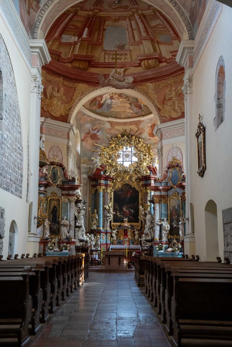 Zdjęcie przedstawia wnętrze kościoła rzymskokatolickiego pw. św. Lenoarda w Lubiniu. Wnętrze kościoła jest barokowe. Można zauważyć liczne zdobienia na ścianach i suficie. Widoczny dwukondygnacyjny ołtarz z licznymi rzeźbami aniołów i świętych, złoceniami i ciemnym obrazem ołtarzowym w centralnej części.