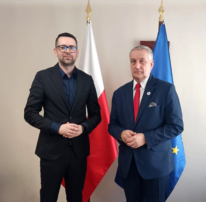 Fotografia przedstawia dwóch mężczyzn stojących na tle flagi Polski oraz UE
