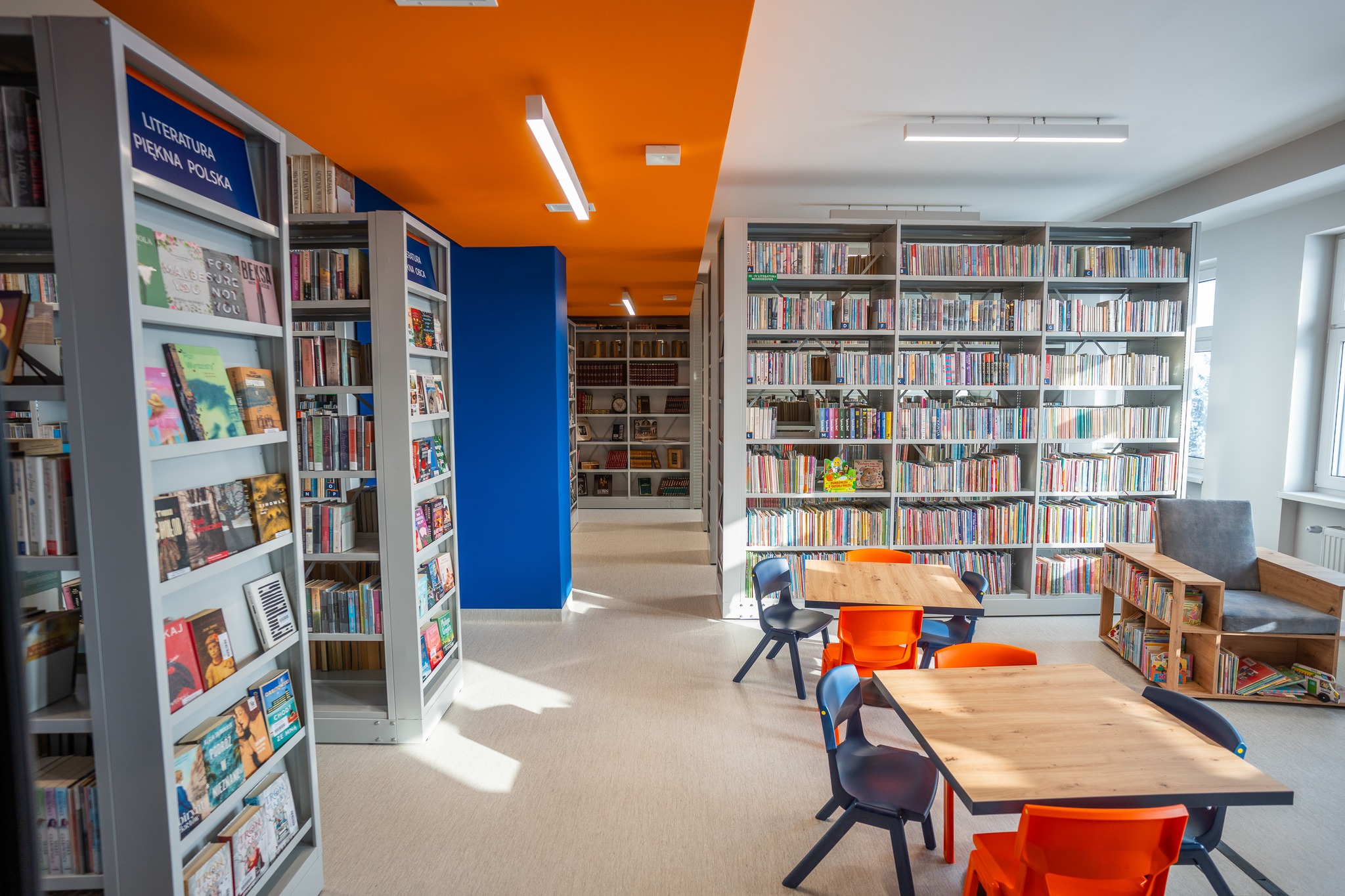 Wnętrze odremontowanej biblioteki. Widoczne regały z kolorowymi książkami oraz stoliki i krzesełka.