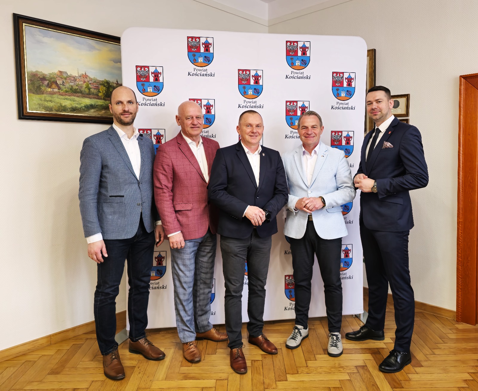 Grupa osób stojących na tle ścianki z logotypem Powiat Kościański