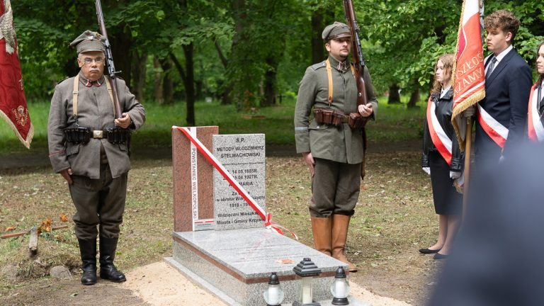 Fotografia przedstawia grób weterana i pełniących przy nim wardę honorową dwie osoby oraz poczet sztandarowy. Uroczysty i podniosły klimat.