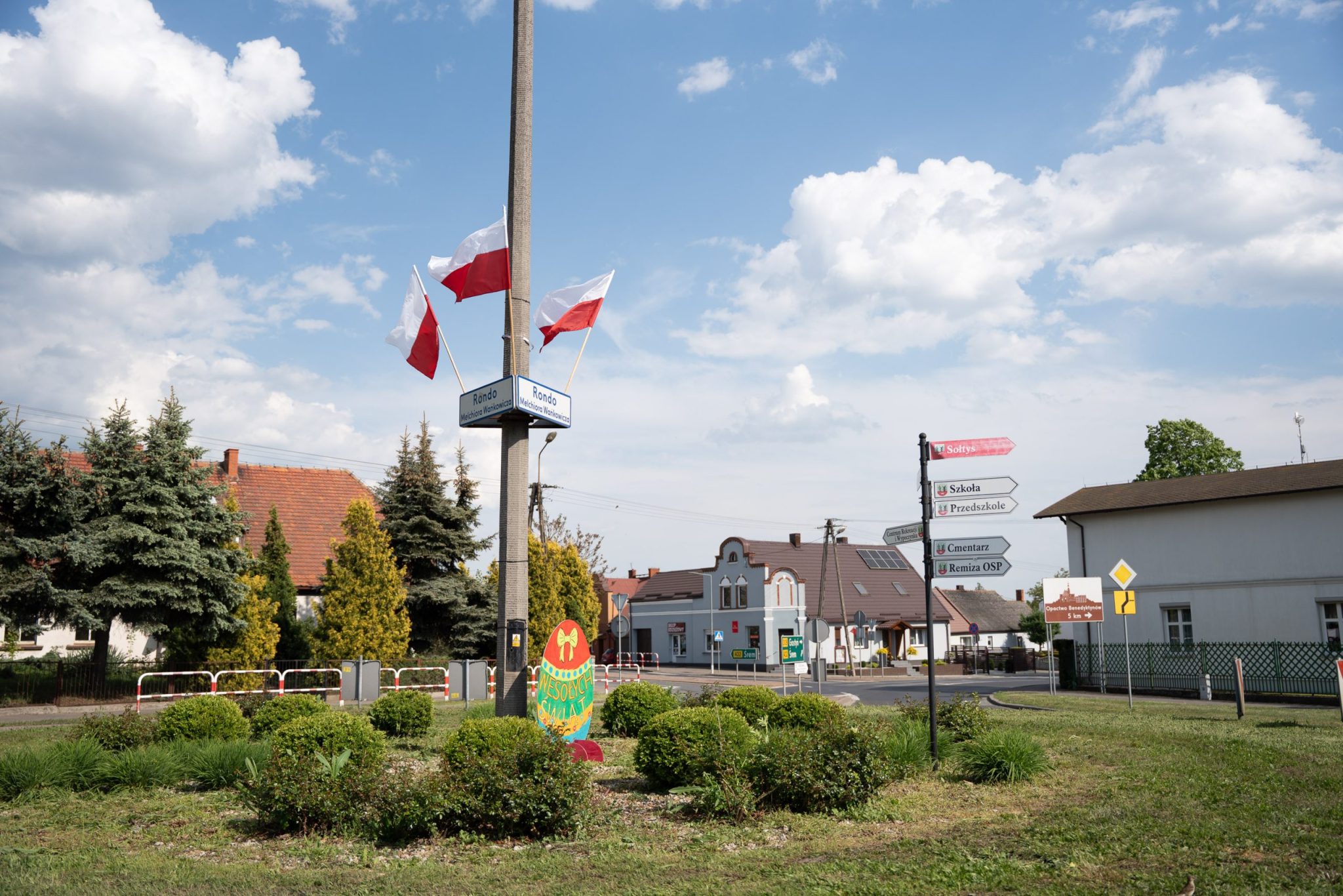 Polskie flagi powiewające na wietrze, zawieszone na słupie w centralnym miejscu miasteczka.