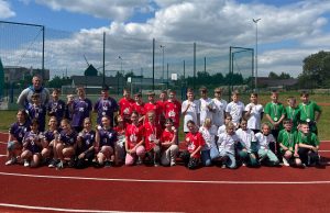 Fotografia przedstawiająca grupę dzieci na stadionie lekkoatletycznym, w sportowych strojach, z medalami w dłoni