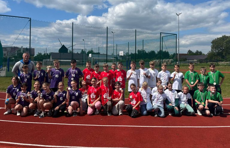 Fotografia przedstawiająca grupę dzieci na stadionie lekkoatletycznym, w sportowych strojach, z medalami w dłoni